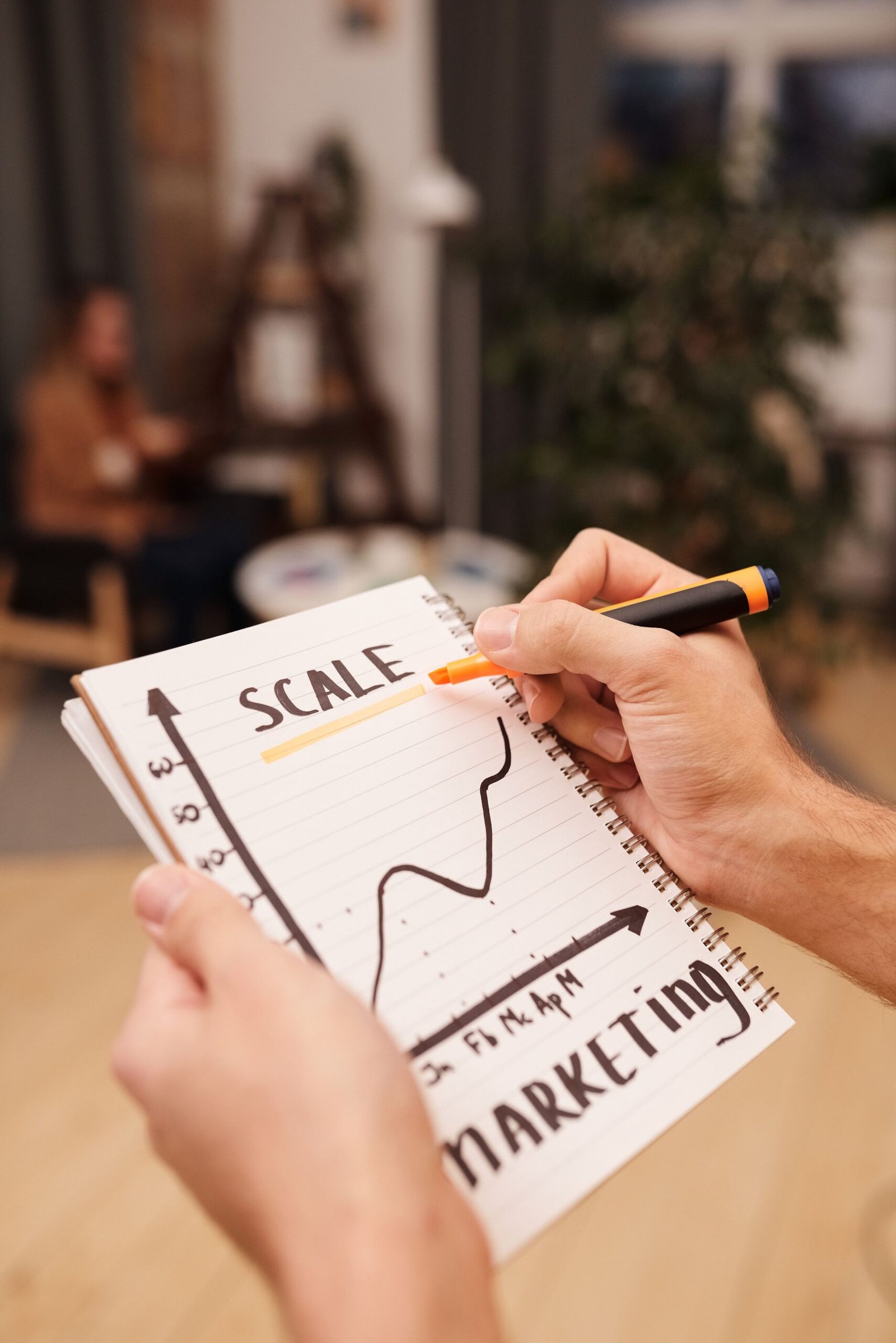 A person draws a marketing scale graph on a notebook with a marker.